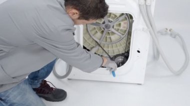 Bir tamirci çamaşır makinesindeki tamburları tamir ediyor. O farklı araçlar kullanıyor ve şu anda o bir tornavida kullanıyor.