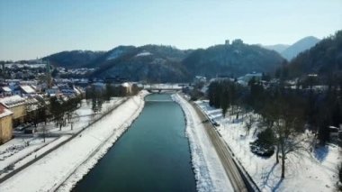 Savinja Nehri'nin her iki yakasında da çok kar var. Kış zamanı. Arka planda büyük bir kale görebiliyoruz. Havadan çekim.