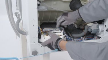 Bir adam bir sorun bulmak ve bir çamaşır makinesi düzeltmek için çalışıyor. Güvenlik eldiveni kullanıyor..