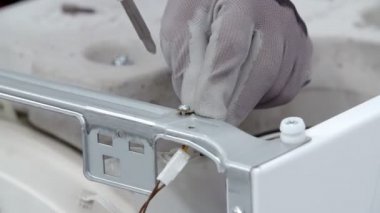 Genç bir tamirci matkap kullanıyor ve yavaşça çamaşır makinesinin bir tarafından vidaları çıkarıyor..
