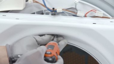 Bir tamirci matkapla vidayı sökmek üzere. Çamaşır ve kurutma makinesini tamir ediyor..