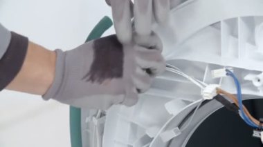 Bir adam çamaşır makinesinin kapısının etrafındaki kabloları çıkarmaya çalışıyor. Cihazı tamir ediyor..