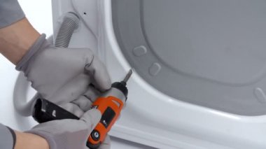 Bir tamirci çamaşır makinesinin arka kapısından vidaları çıkarıyor. Matkap kullanıyor..
