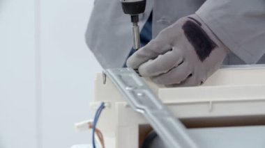 Bir tamirci matkapla vidaları çıkarıyor ve güvenlik eldiveni giyiyor..