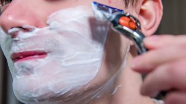 Genç bir adam banyoda tıraş oluyor. Yüzünde bir sürü köpük var..