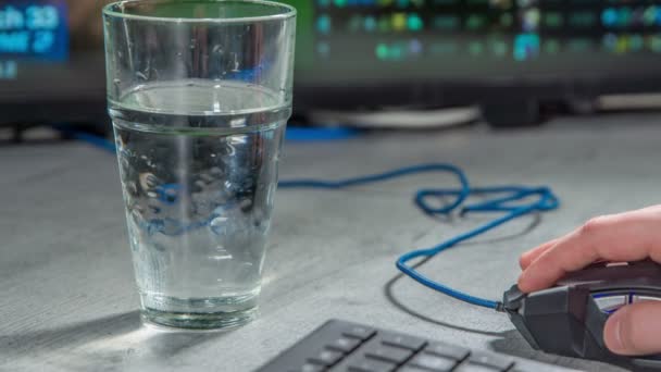 若い男がコンピュータのマウスを動かし その後 彼は水を一口飲んでいます 彼は何かに取り組んでいる — ストック動画