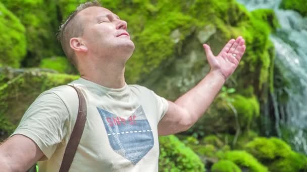 Ein Mann Sitzt Auf Einem Felsen Neben Einem Wasserfall Und — Stockvideo