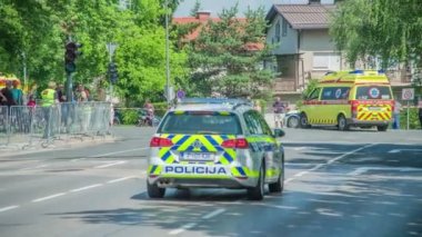 Bisiklet yarışçılarının önünde iki polis arabası ve bir ambulans sürüyor..