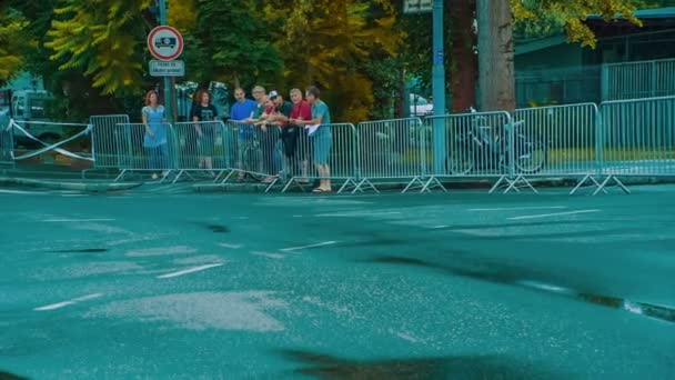 フェンスの反対側の人々は通り過ぎるスポーツマンのために拍手している 雨のため道路はぬれている — ストック動画