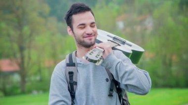 Genç bir adamın omzunda gitarı var ve gülümsüyor..