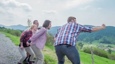 A group of friends is standing by the side of the road. One of them is holding his cell phone. When they all jump up in the air, he takes a selfie of them all. The nature around is gorgeous.The weather is fantastic.