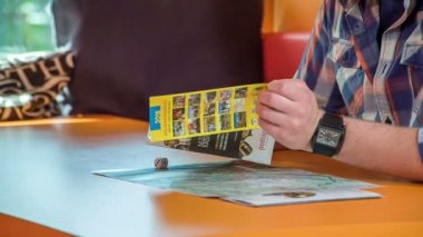 Genç bir adam önündeki masada duran broşürü kontrol ediyor..