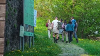 Bir grup genç turist birkaç tahtanın yanından geçiyor ve yokuş yukarı devam ediyorlar..