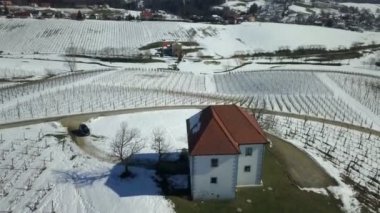 Karlı bir manzara ve tepenin üstünde yalnız bir ev görebiliyoruz. Hava görüntüsü. Etrafta üzüm bağları da var..