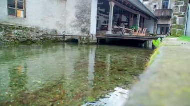 Su büyük bir evin altından akıyor. Verandada sandalyeler ve masalar var. Bu Slovenya Karst 'ında gerçekleşiyor