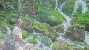 Bir adam güzel bir şelaleyi ve muhteşem yeşil bir doğayı gözlemliyor..