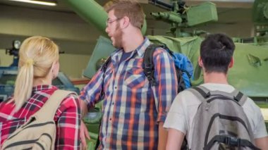 Genç bir adam bir müzedeki askeri tankı işaret ediyor. İki arkadaş onu izliyor..