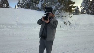 Bir adam karın üzerinde duruyor ve kamerasıyla bir şeyler çekiyor..