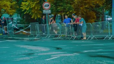 Birkaç yetişkin çitin arkasında dikilip bisikletçilerin geçmesini bekliyor..