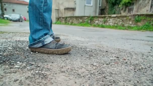一个穿牛仔裤的男人站在路上环顾四周 他周围有许多旧房子 — 图库视频影像
