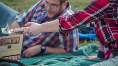 Gençler fındık ve çikolata yiyorlar ve güzel bir doğanın ortasında battaniyenin üzerinde oturuyorlar..