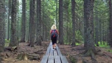 Genç kadın ormanda ahşap yolda yürüyor.