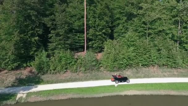 湖のそばの道をヴィンテージカーが走っている 背景には大きな森があります 空中射撃 — ストック動画