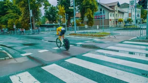 自転車レーサーがゼブラクロスを通って自転車に乗っていると群衆を通過しています 寒い雨の日だ — ストック動画