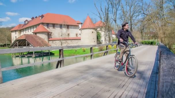 在城堡附近的桥上骑自行车的年轻人的镜头 — 图库视频影像