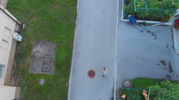 誰かが村の真ん中の路上でキックスクーターに乗っています 空中射撃 — ストック動画