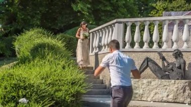 Güzel bir gelin parktaki merdivenlerden iniyor ve bir fotoğrafçı onun fotoğraflarını çekiyor..