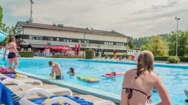 DOMZALE, SLOVENIA - 20. HAZİRAN 2015 Bir kız güverte sandalyesinde dinleniyor ve yüzme havuzunda eğlenen arkadaşlarını izliyor.