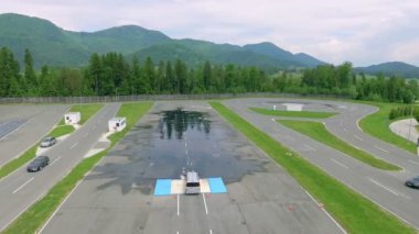 Güvenli bir sürüş merkezinde büyük bir su birikintisinde araba sürüyor. Sola ve sağa doğru hareket etmeye başlıyor. Hava görüntüsü.