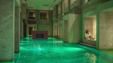 RIMSKE TOPLICE, SLOVENIA - 15. Eylül 2018. Yüzme havuzunun köşesinde oturan genç bir kadın sadece bornozunu giyiyor. Bu termal oteldeki havuz boş..