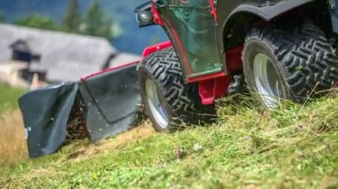 Traktörlü bir çiftçi yokuş aşağı gidiyor ve büyük bir tarım makinesiyle çimleri kesiyor..