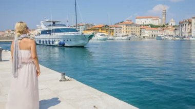 Yazlık elbiseli genç bir kadın iskelede duruyor ve büyük bir sürat teknesi yaklaşıyor..