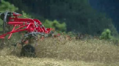 Genç bir çiftçi dağlardaki büyük bir çim tarlasında saman hazırlıyor. Döner tırmıklar çok hızlı hareket ediyor..