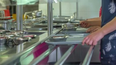 Okul çocukları okul kantinindeki tepsilere yemek koyuyorlar. Onlar da tatlı ve çay içiyorlar..