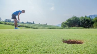 Bir kadın golf sopasıyla nazikçe golf topuna vuruyor ama golf topu hala boş bir deliğe girmiyor..
