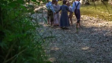 Çocuklar nehrin kıyısında dans ediyorlar. Birbirlerinin elini tutuyorlar ve geleneksel kıyafetler giyiyorlar..