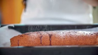 Bir öğretmen pastaya biraz beyaz şeker serpiyor. Aşçılık sınıfındaki öğrenciler lezzetli bir tatlı yaptılar ve şimdi onu yiyecekler..