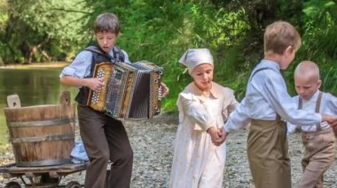 Mutlu çocuklar dans ediyor ve içlerinden biri akordeon çalıyor. Nehir kenarında güneşli güzel bir gün..
