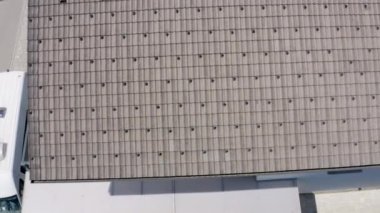 Evin gri çatısı. Kasabada güneşli bir gün. Beyaz bir minibüs evin dışında park halinde. Hava görüntüsü.