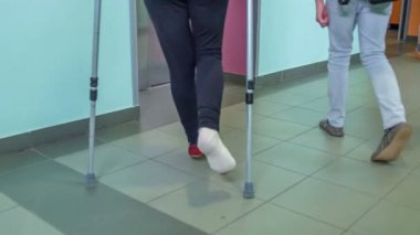 Genç bir öğrenci ve arkadaşı bir okul binasındaki asansöre yaklaşıyorlar. Bacağı alçıda..