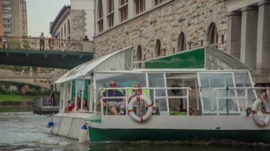 Turistler Ljubljanica nehrinin karşısındaki bir teknede tura çıkıyorlar. Yaz mevsimindeyiz. Dışarıda kalmaktan zevk alıyorlar..
