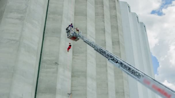 2人の消防士がビルの壁に登るときに負傷した登山家に連絡しようとしています — ストック動画
