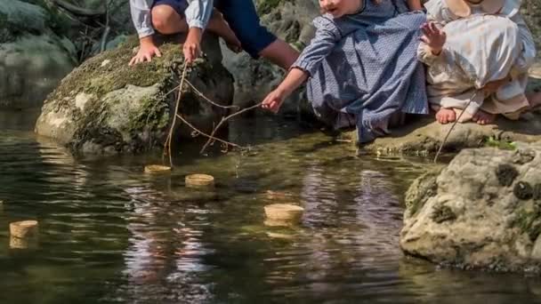 小さな子供たちが川の水面を泳いでいるアイテムに触れようとしています 女の子は小さな枝を手に持っています — ストック動画