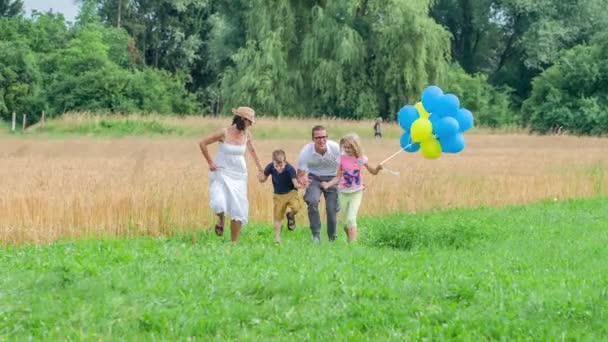 美しい若い家族を見ることができます 両親と子供たちは一緒に屋外で時間を過ごしていて 風船を運んだり笑ったり運んだりしています — ストック動画
