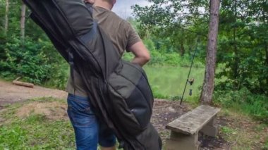 Genç bir balıkçı bir lke 'a ulaşıyor ve ağacın yanına bir balıkçı malzemesi koyuyor..