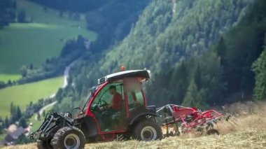 Çiftçiler dik tepelerde saman hazırlıyorlar. Arka planda dağlar ve vadiler var..